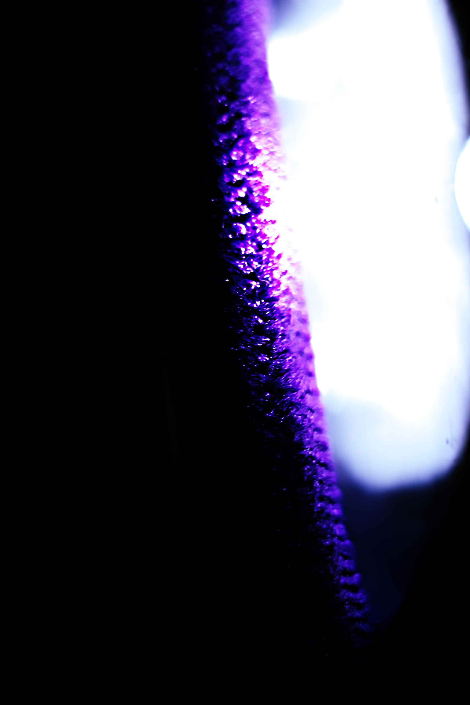 Abstract photo with darkness on the left side, a patterned line of purple near the middle and a orb of white light on the right side with a small circle in the middle
